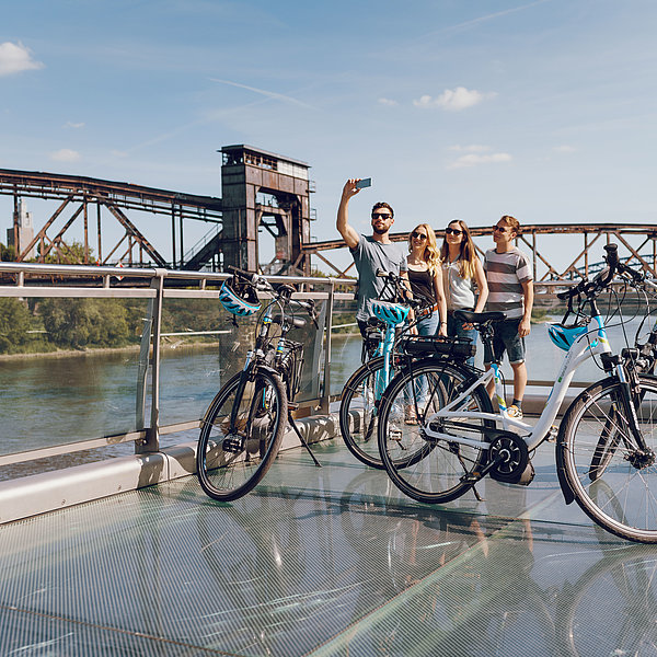 Eine Gruppe fotografiert sich auf einer SWM E-Bike-Tour vor der Hubbrücke in Magdeburg an der Elbe.