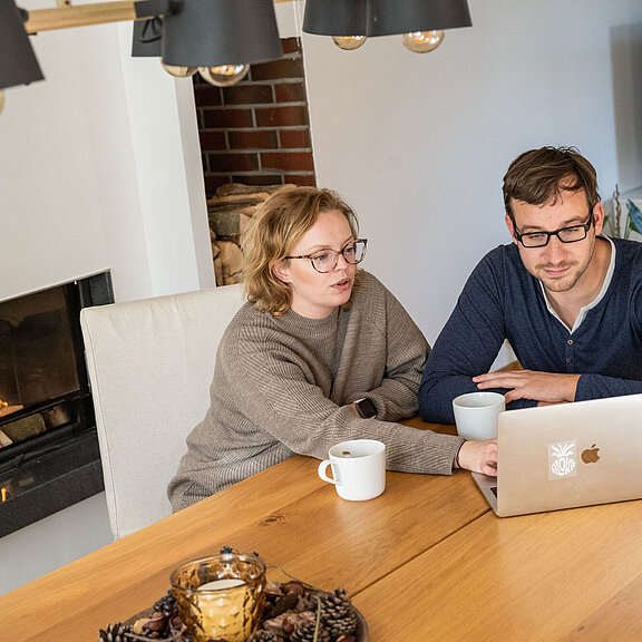 Ehepaar sitzt am Tisch und arbeitet gemeinsam am PC