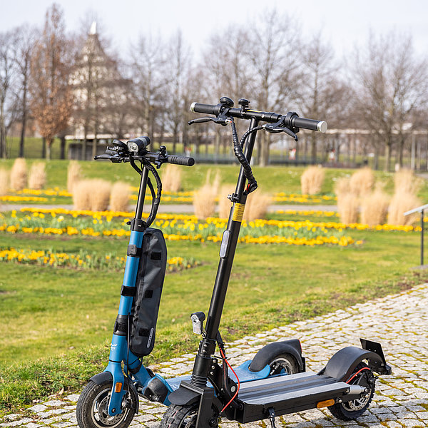 Zwei SWM E-Scooter stehen im Elbauenpark. Im Hintergrund ist der Jahrtausendturm zu sehen.